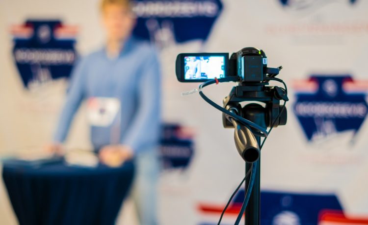 a person standing behind a microphone with a cell phone on a tripod